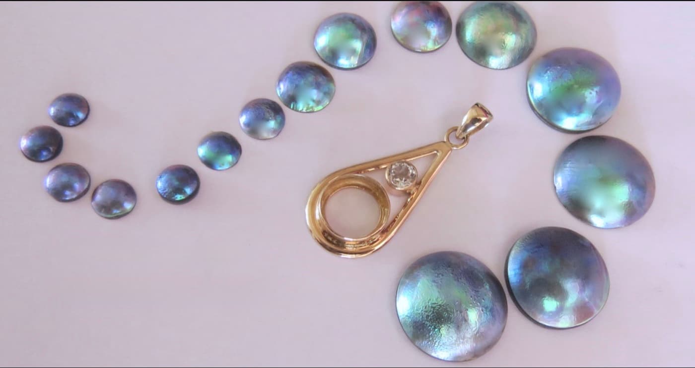 Loose New Zealand blue paua pearls beside a gold pendant setting
